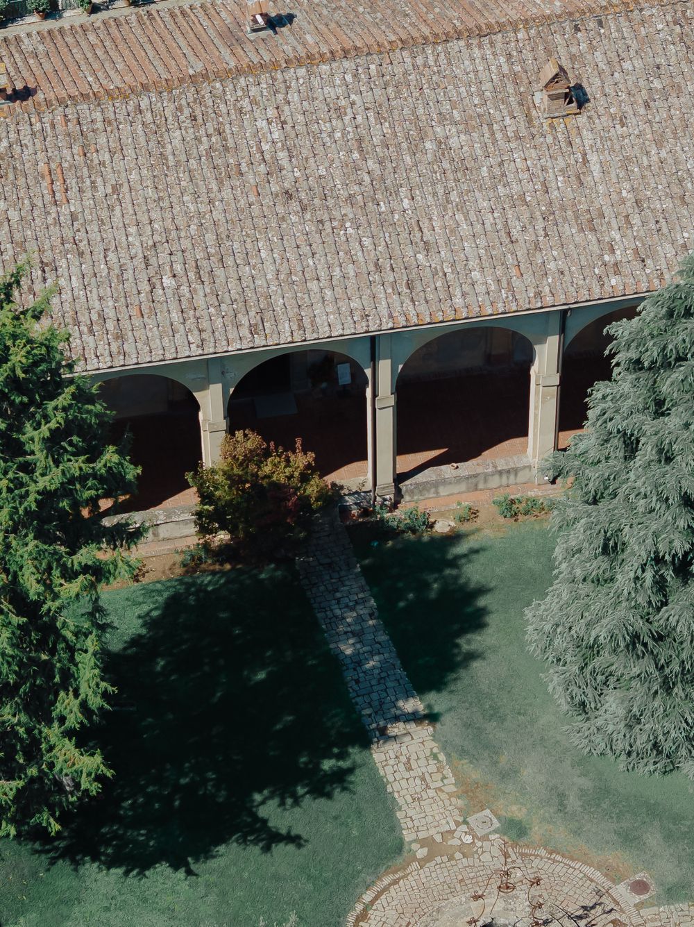 Drone shot of an elegant outdoor venue with brick colonnade and manicured gardens.