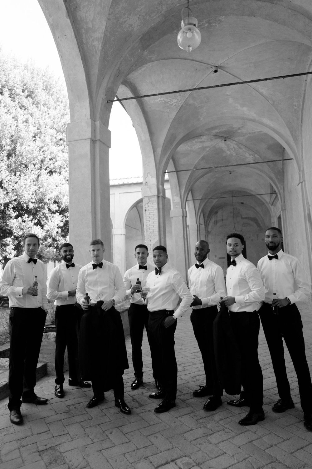 Groomsmen in formal black and white attire posing under elegant archways.