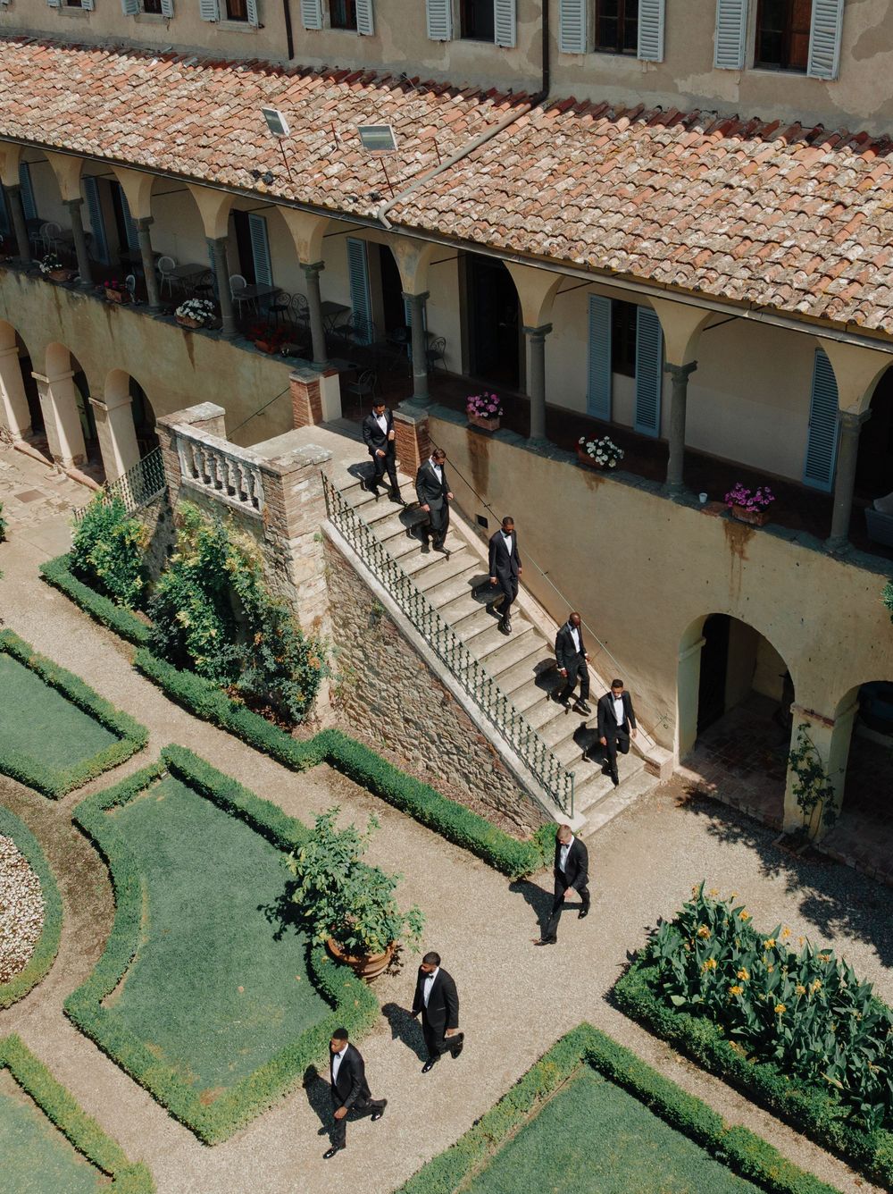Aerial view of formal-dressed guests descending stone stairs in a Mediterranean courtyard garden.