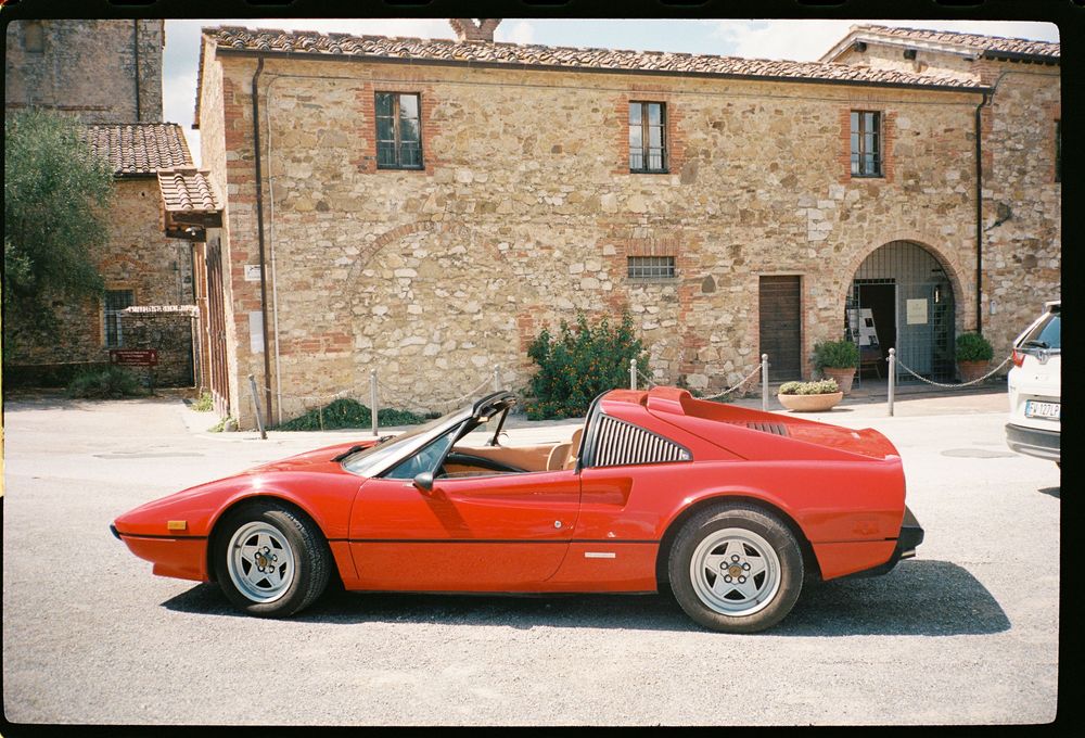 A row of vintage red Ferrari sports cars parked in front of an old stone building facade.