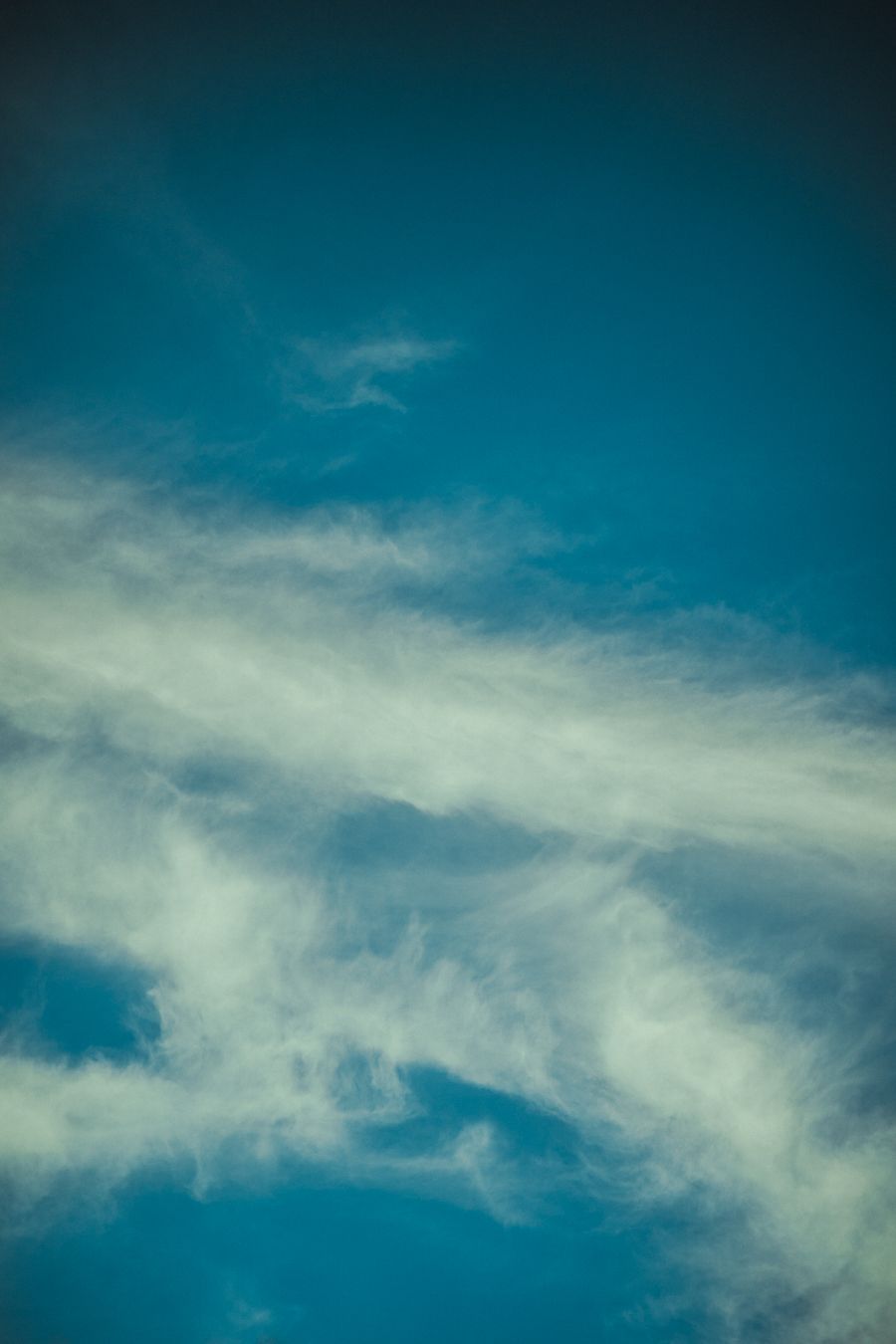 Wispy white clouds drift across a deep turquoise blue sky creating a dreamy atmospheric backdrop.