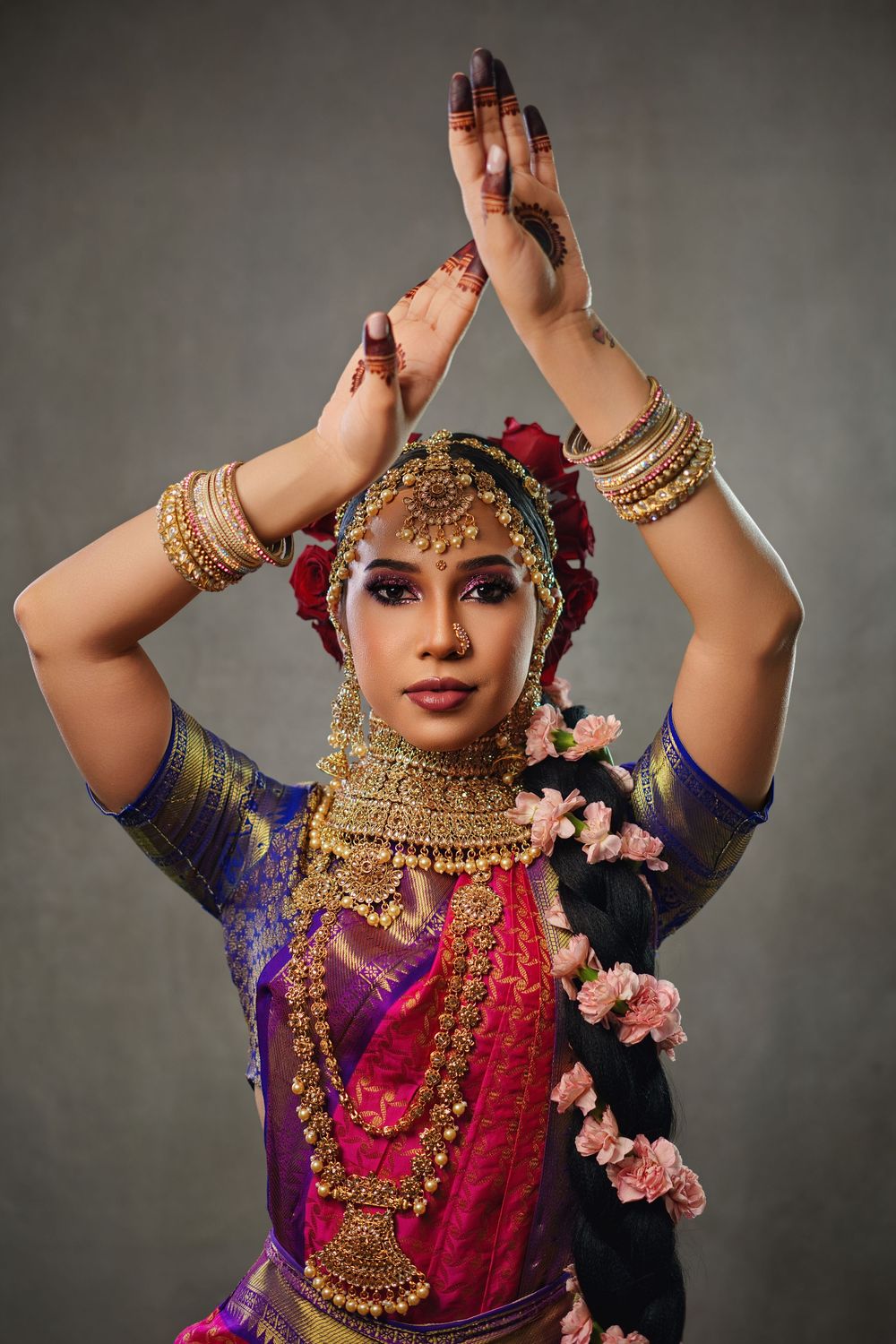 Traditional Indian dancer wearing ornate gold jewelry and purple attire performs elegant dance movements.