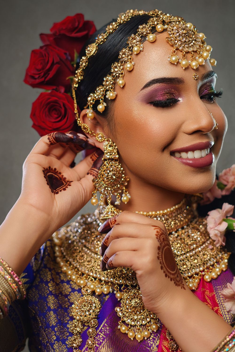 Traditional South Asian bridal jewelry and makeup with ornate gold necklace and red roses in hair.