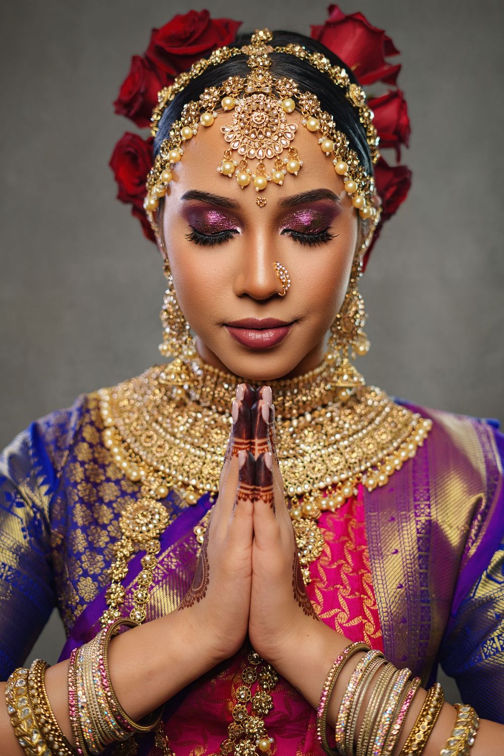 Classical Indian dancer in prayer pose wearing ornate gold jewelry and purple silk costume.