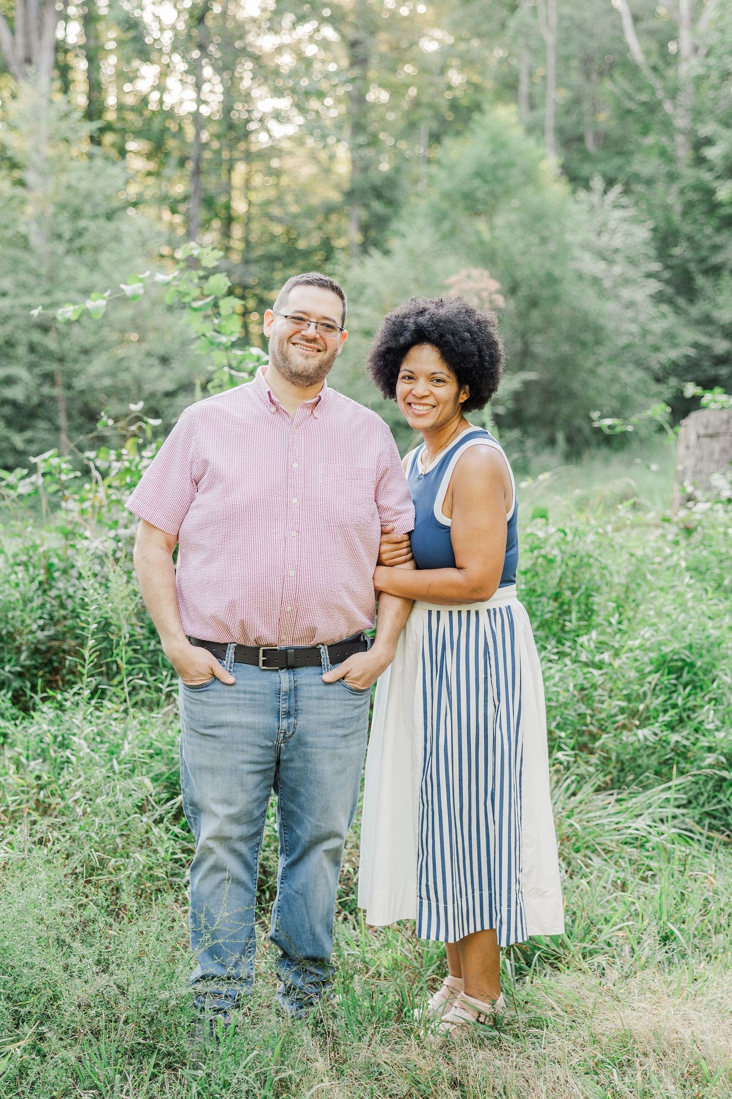 Couple posing together in casual attire against natural woodland backdrop.