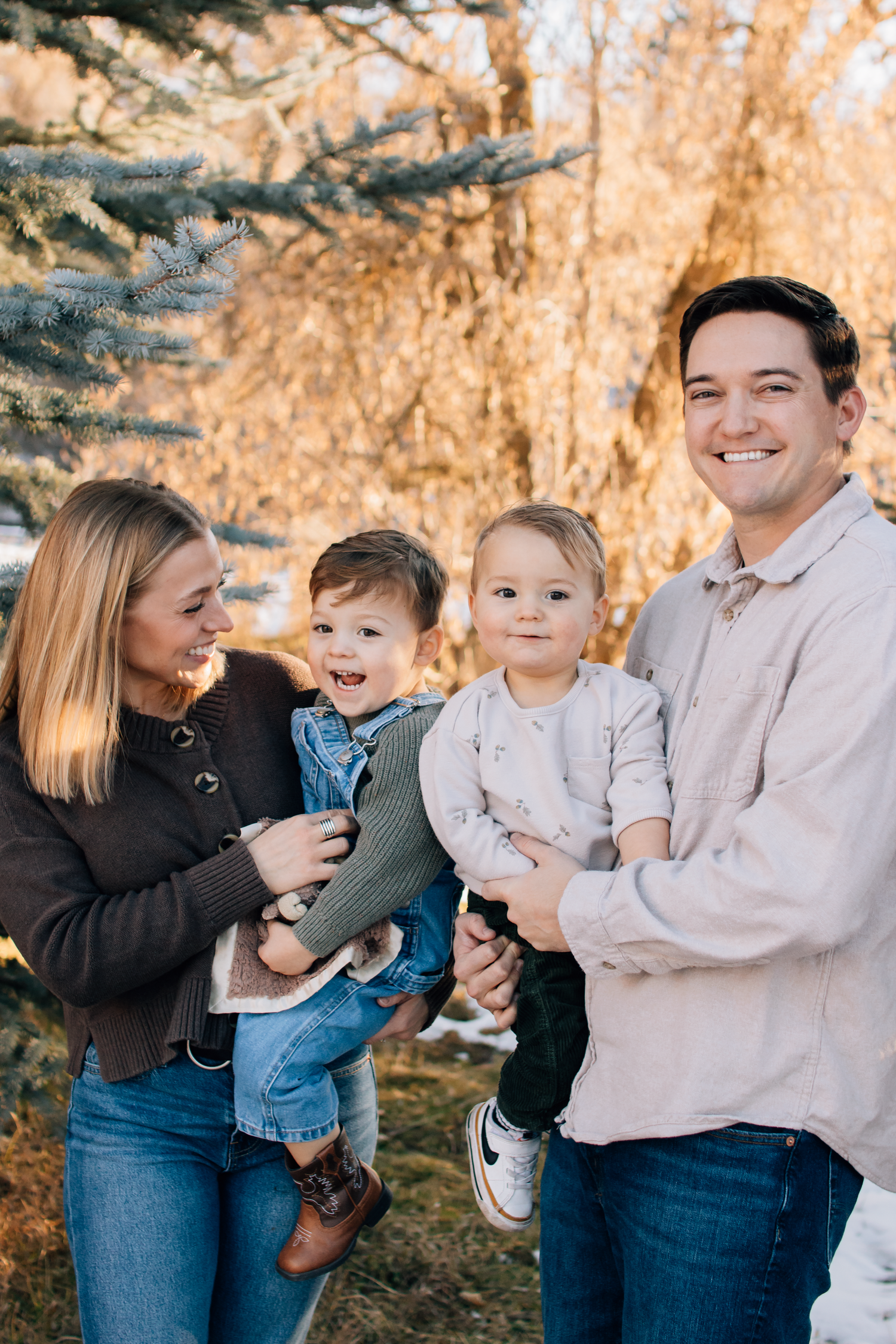 A family enjoys a warm autumn day outdoors together with fall foliage and evergreen trees in the background.