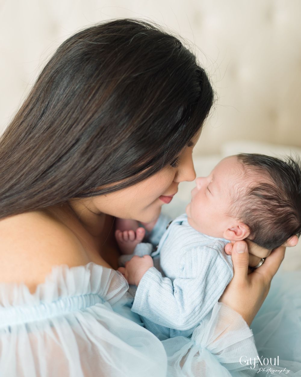 A tender moment between mother and baby captured in a series of gentle kisses and nuzzles against a light background.