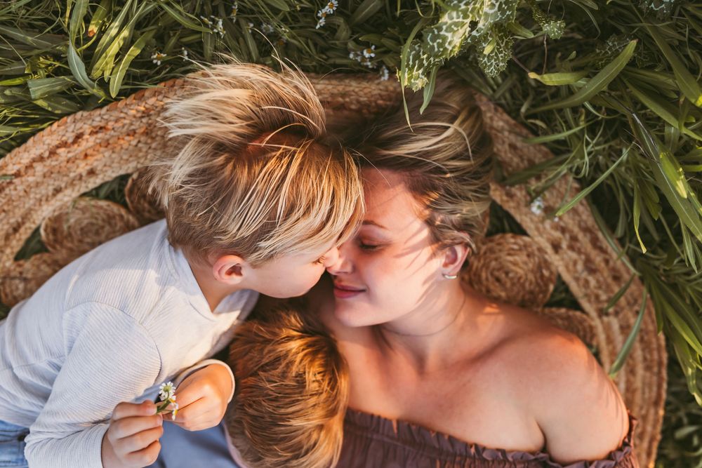 Tender moment shared between two people lying on ground with green foliage overhead in natural light.