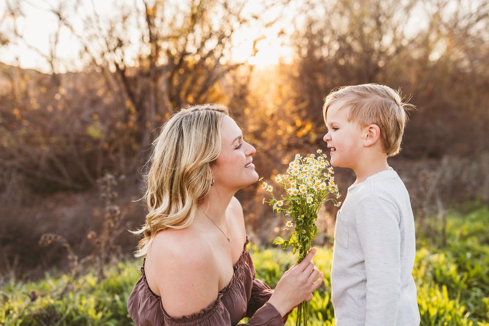 Mother and son share a tender moment in a sunlit field with yellow wildflowers at golden hour.