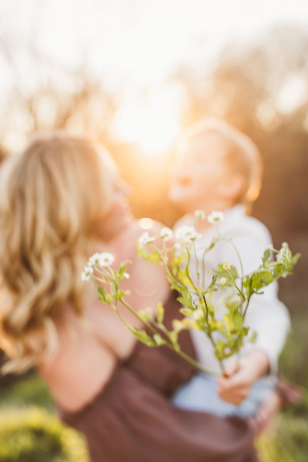 Child smelling small white flowers in a garden during golden hour with soft bokeh background.