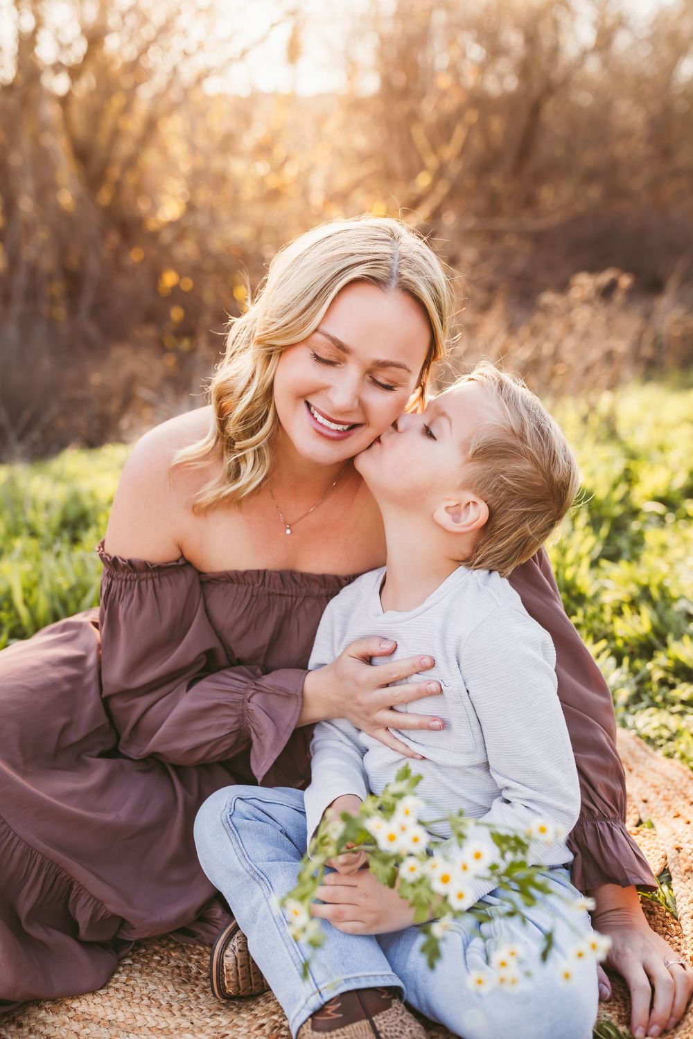 A tender moment between parent and child sitting on a blanket outdoors during golden hour with spring flowers nearby.