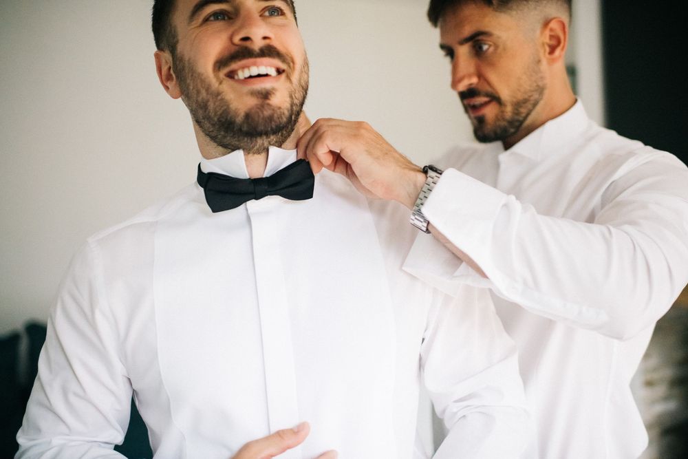 Wedding preparation scene with formal attire adjustments in natural light.