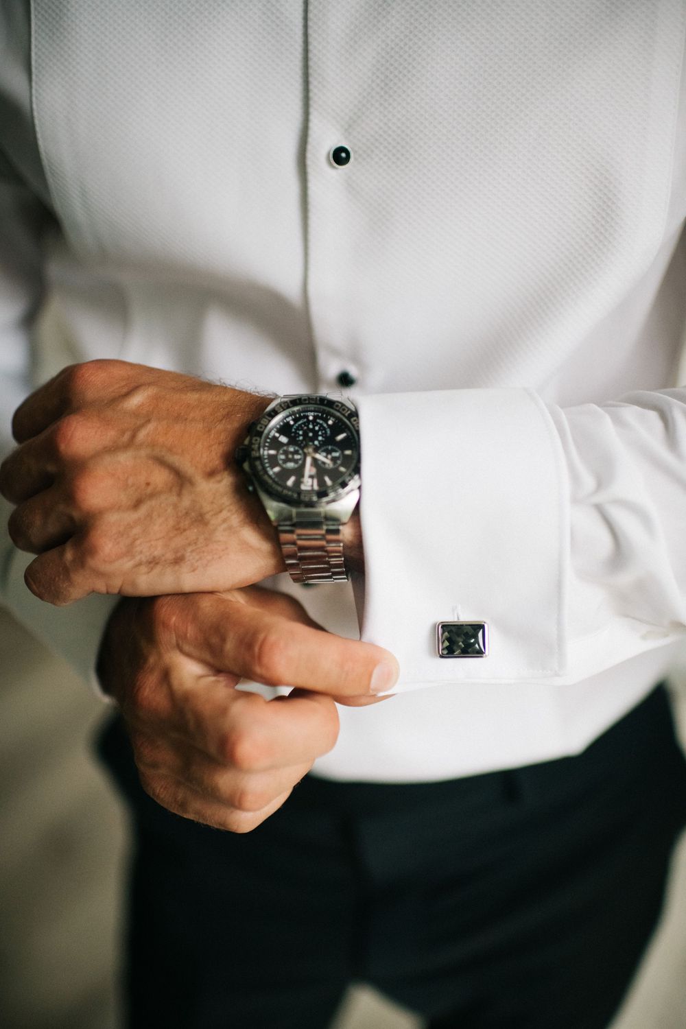 Close-up shots of hands adjusting silver watch and white dress shirt cuffs.