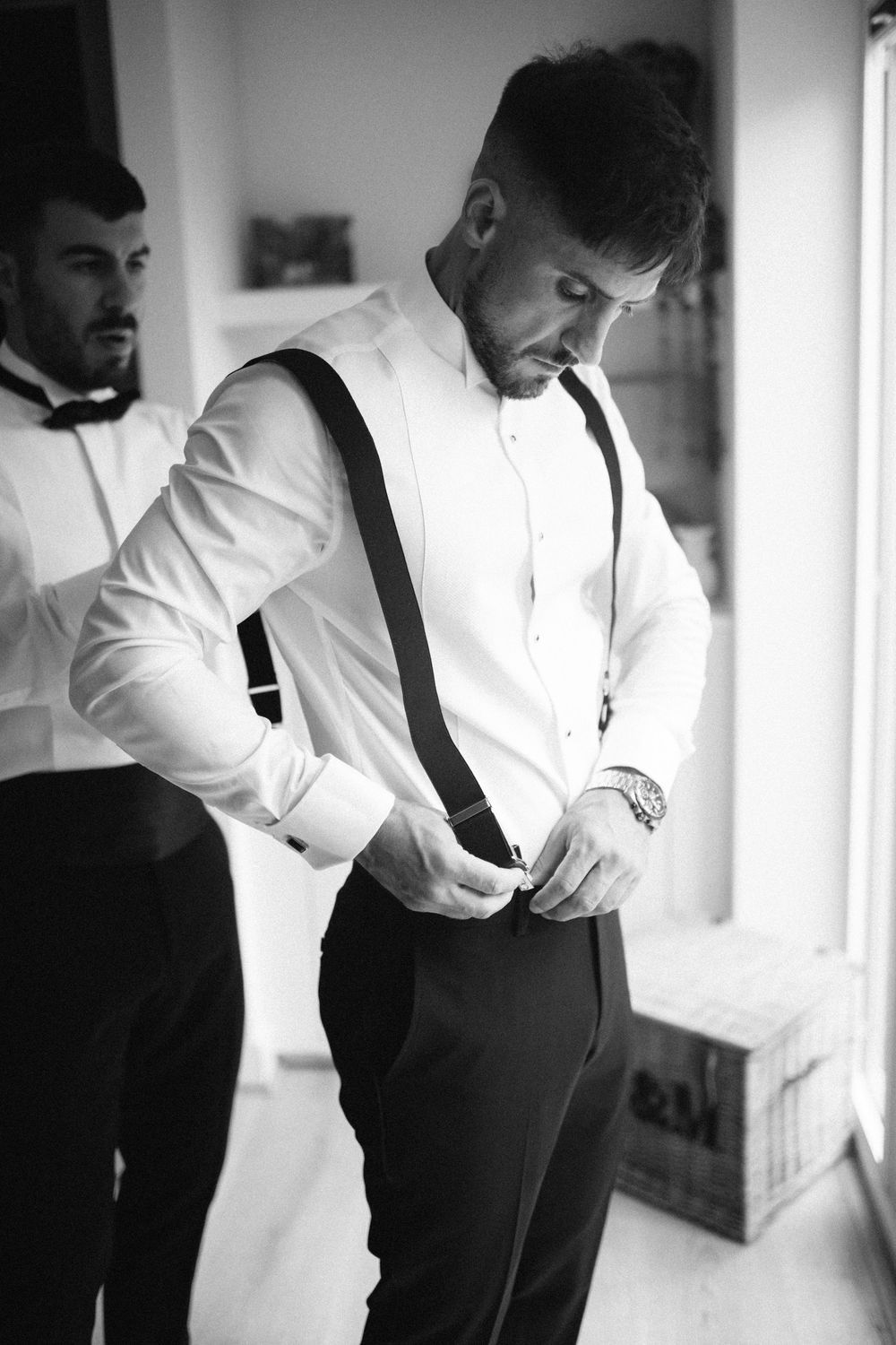 Black and white photo of formal attire preparation with suspenders and dress shirt.