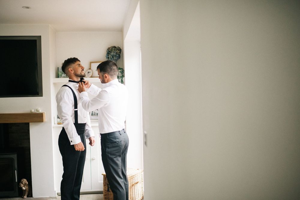 Wedding preparation scene showing formal attire adjustments in a bright interior space.