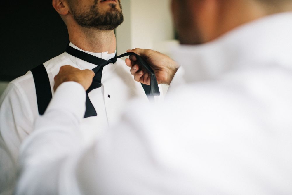 Close-up shot of formal bow tie adjustment against white dress shirt.