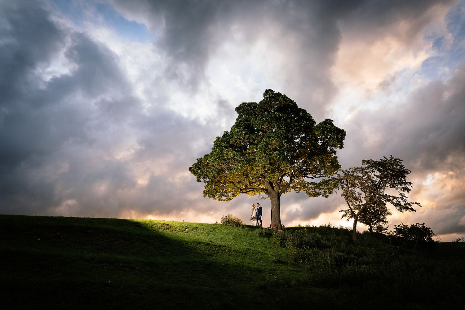 Dramatic storm clouds roll over hillside landscape during golden hour creating moody wedding day atmosphere.