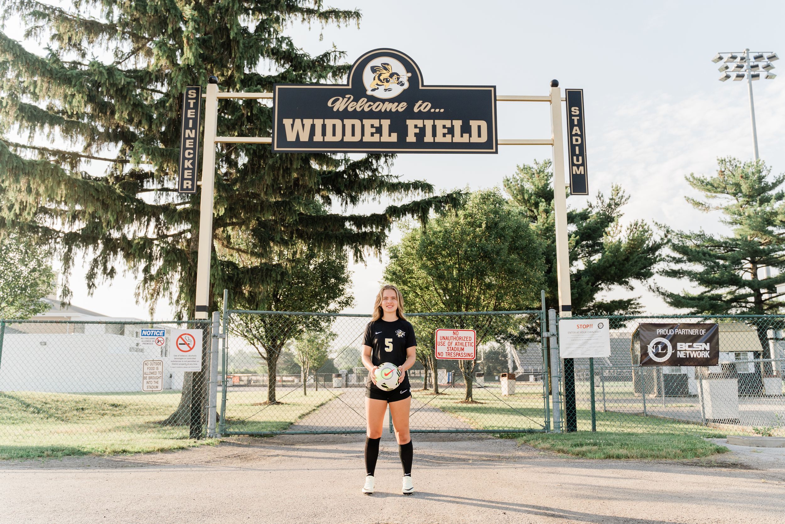 A series of five connected photos showing a baseball field entrance with a Widdel Field sign and evergreen trees.