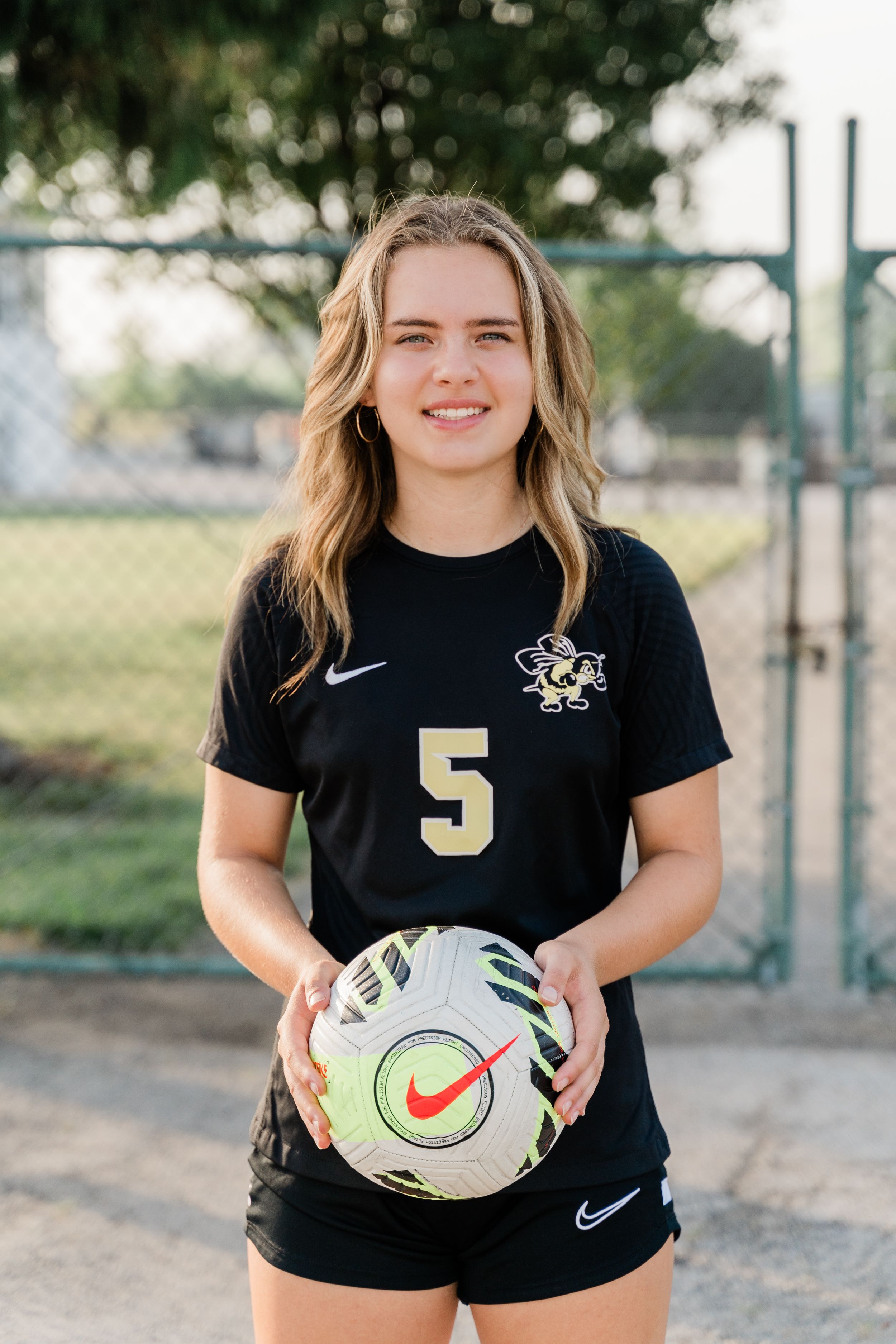 Soccer player in black Nike shirt holds ball while posing for sports photo series outdoors.