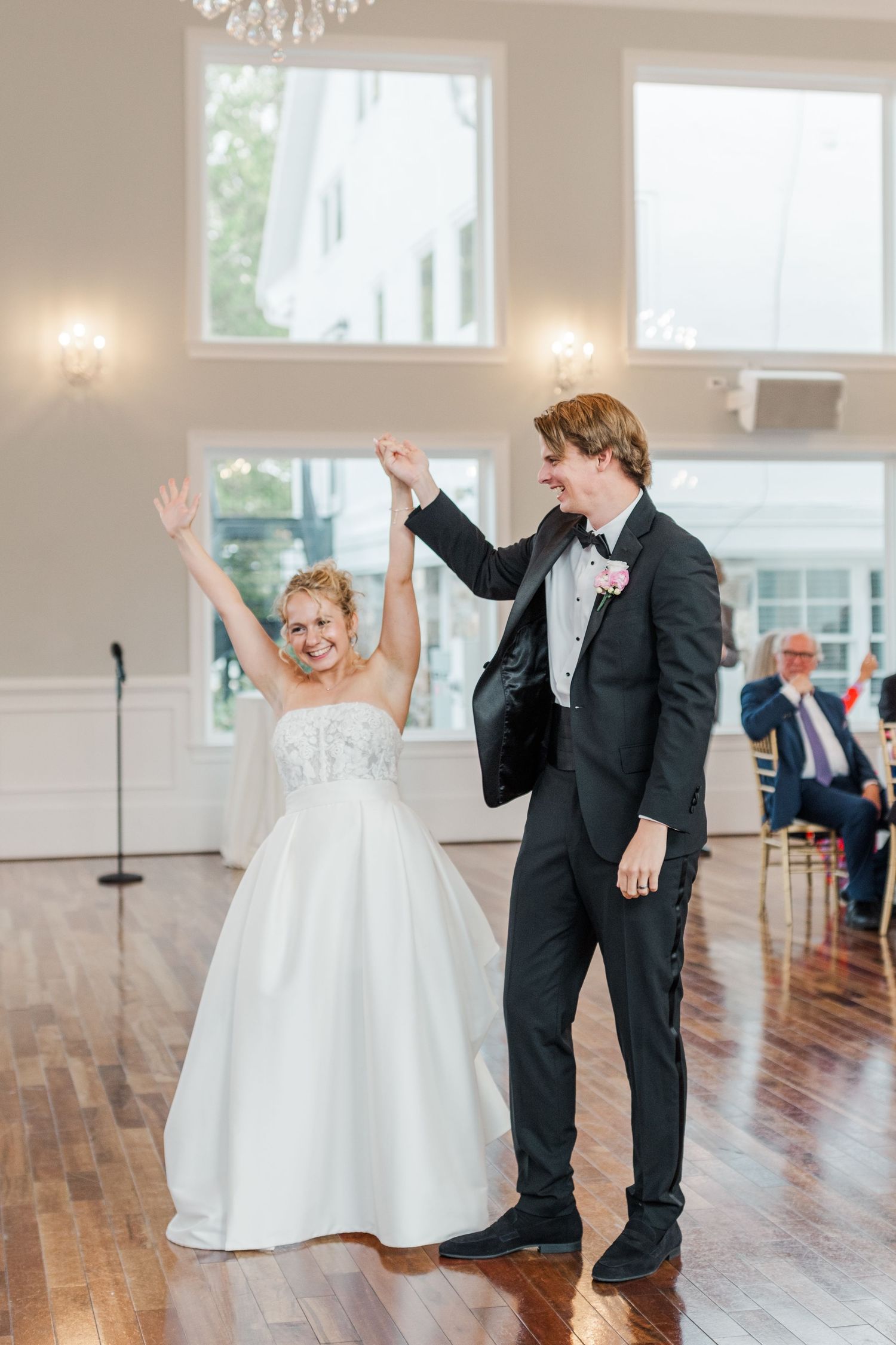 A couple celebrates during their first dance in an elegant white ballroom with hardwood floors.