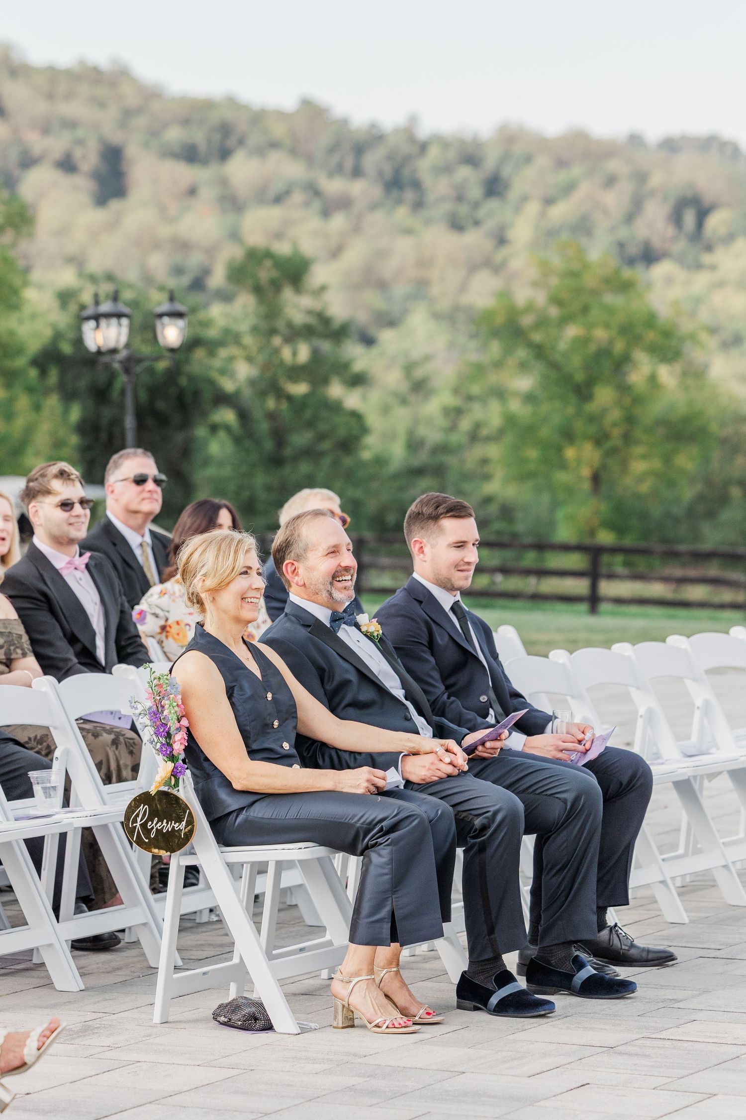 Wedding guests seated in white chairs during outdoor ceremony.