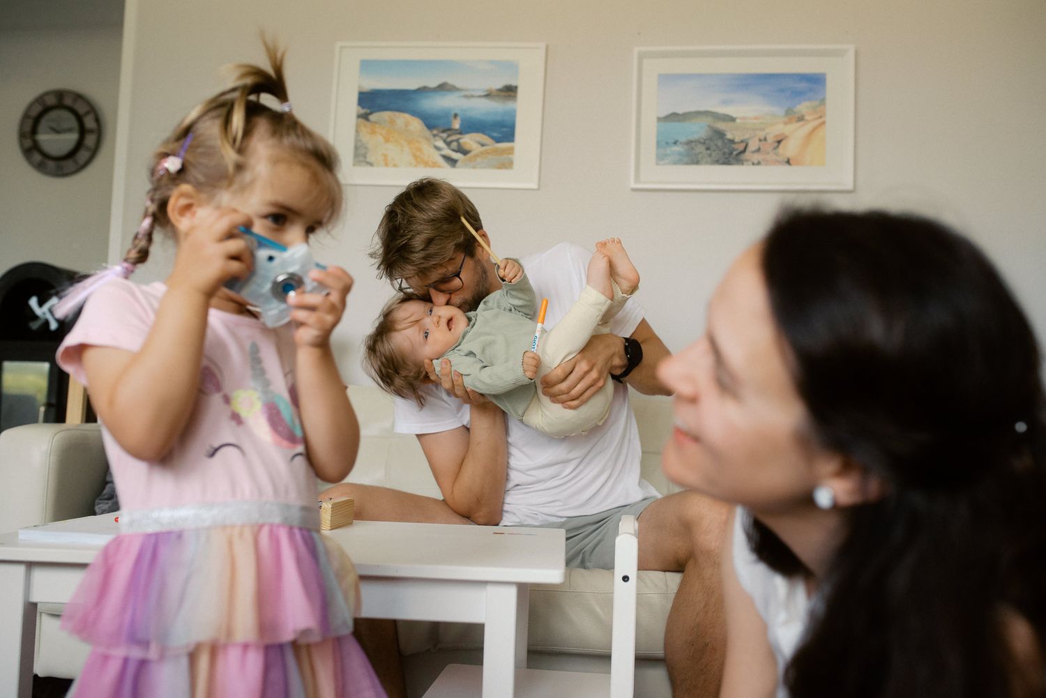 People dance and celebrate together in a joyful group scene with framed artwork visible on the wall behind them.