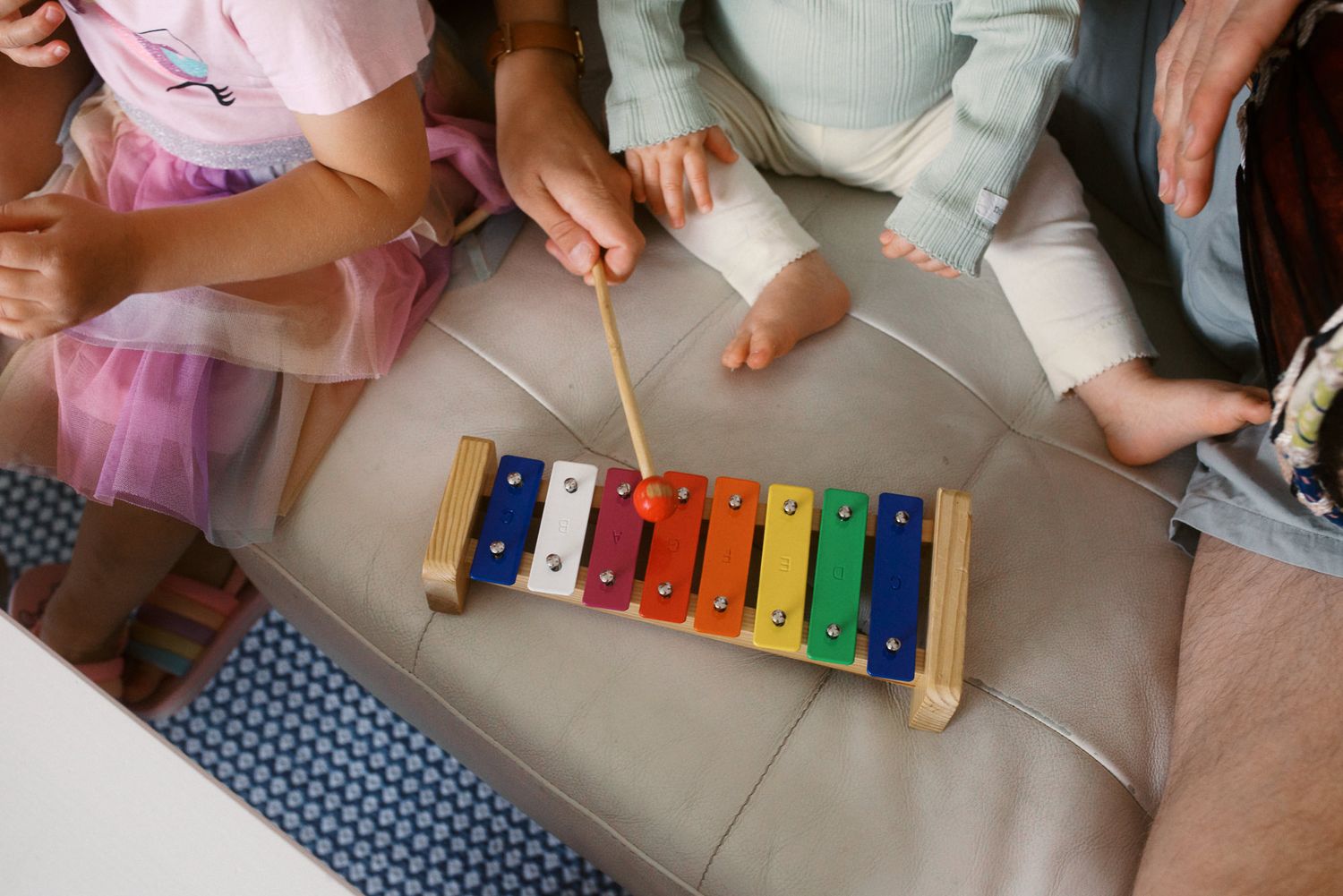 A colorful xylophone being played with wooden mallets on a table with multiple people gathered around it.