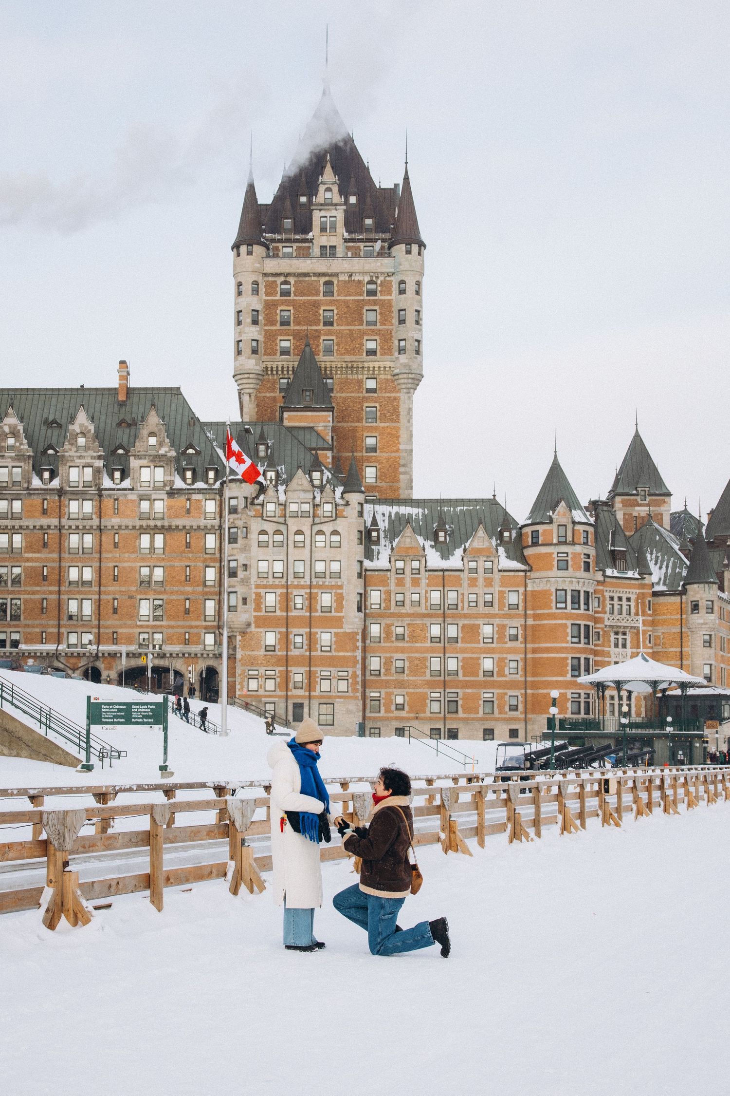 Chateau Frontenac hotel in Quebec City stands majestically against a snowy winter landscape with wooden fences in foreground.