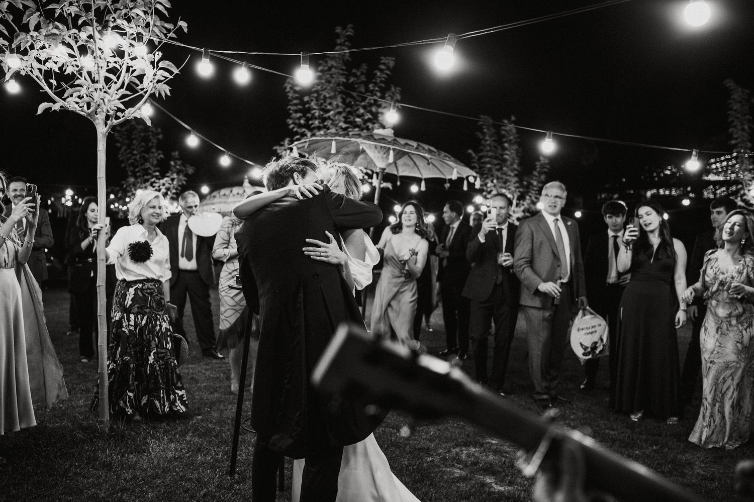 Wedding guests dance and celebrate under string lights at an outdoor evening reception.