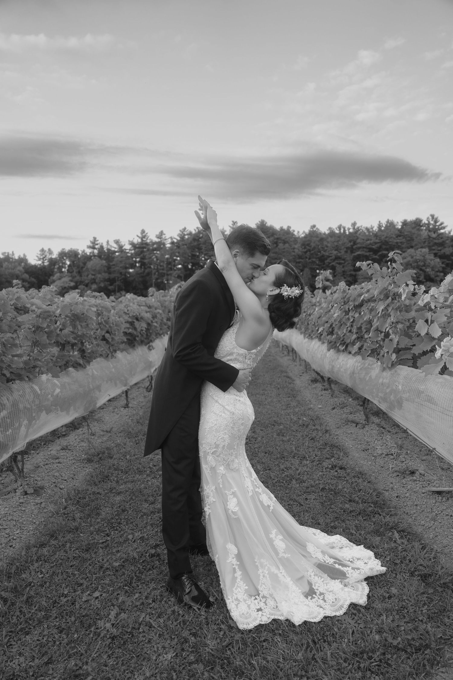 A couple in wedding attire dances together on a scenic path surrounded by greenery in black and white photography.