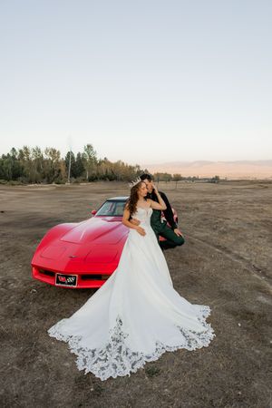 Bride and groom posing together beside a red classic car during a Utah wedding