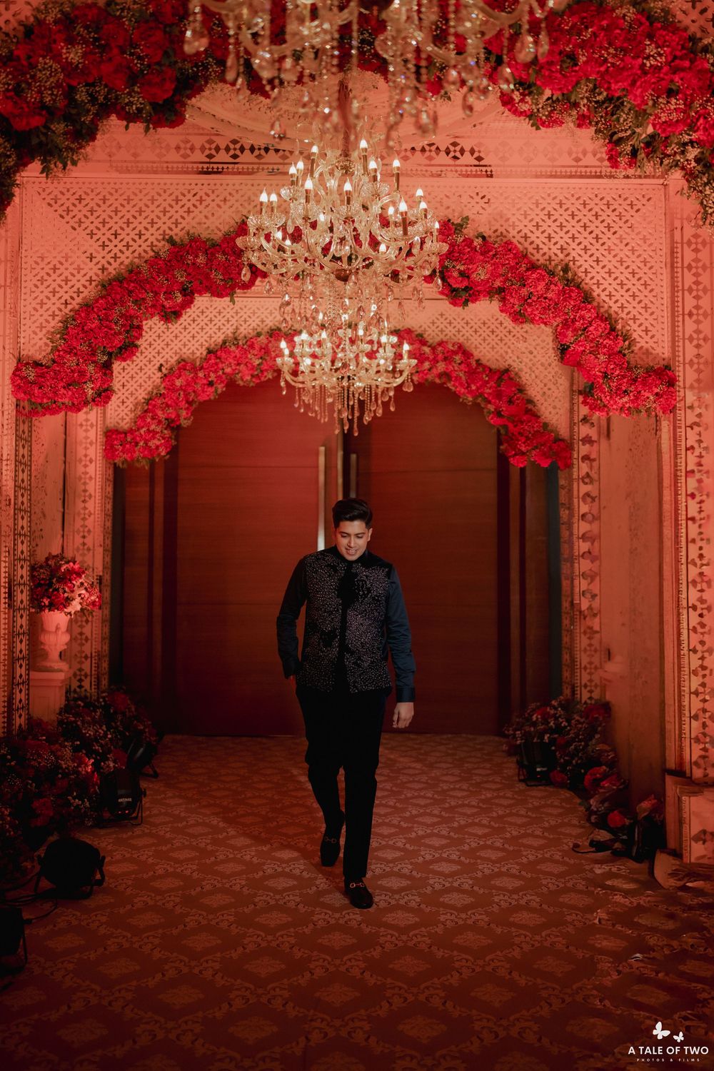 Elegant ballroom decorated with red floral arrangements and crystal chandeliers creates a romantic wedding venue atmosphere.