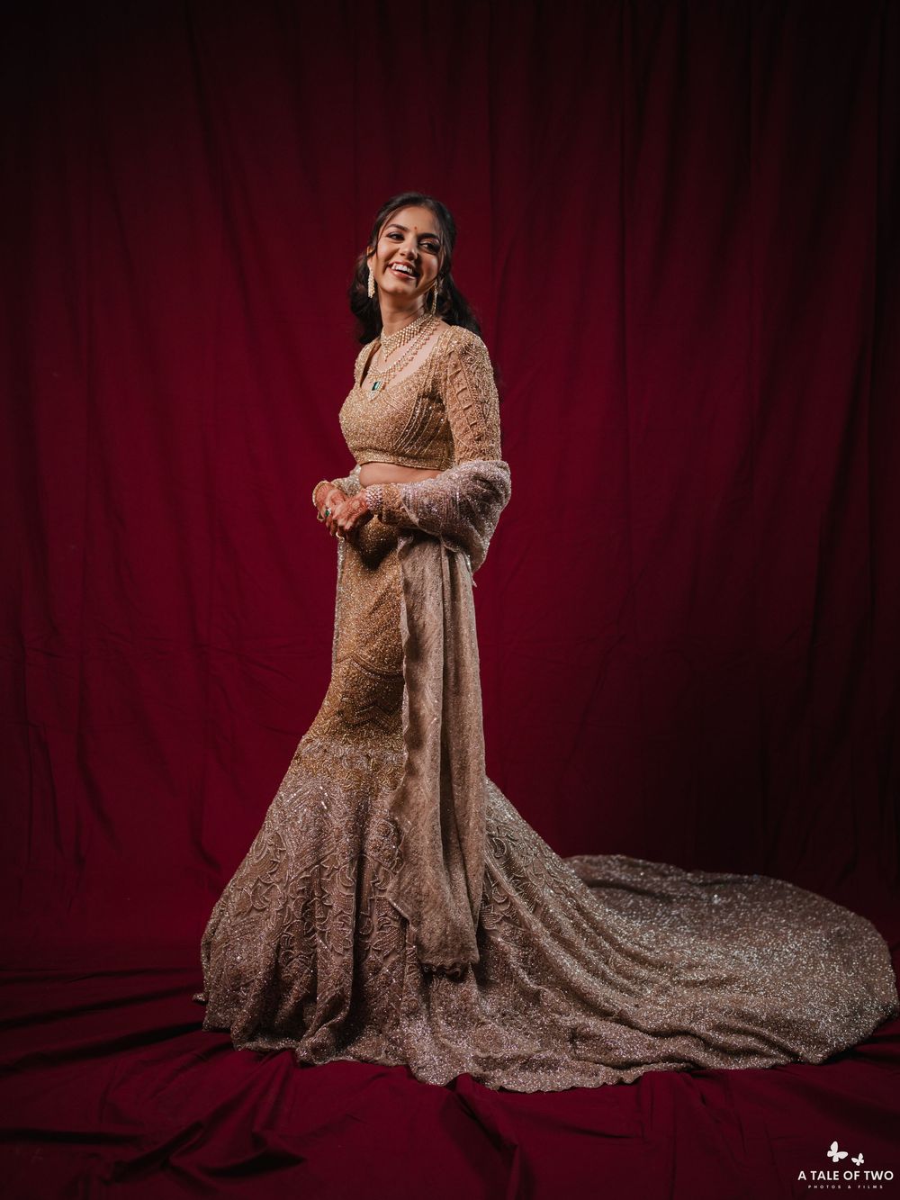 Bridal portraits against a deep red backdrop showcasing an embellished gown with a flowing train.