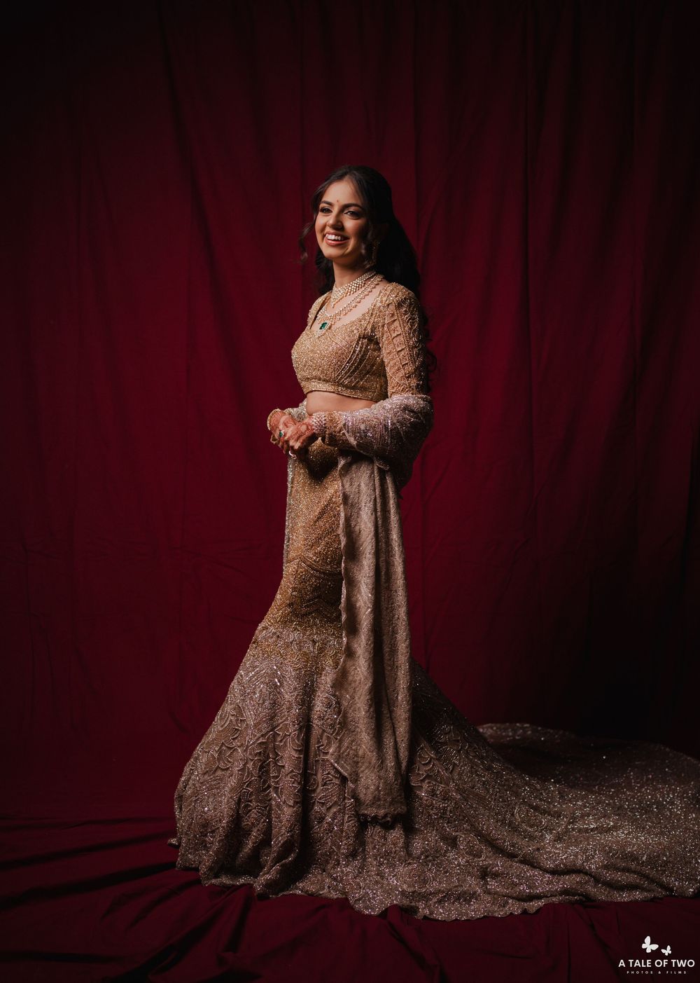 A glamorous portrait session against a deep red velvet curtain backdrop features an elegant evening gown with intricate details.