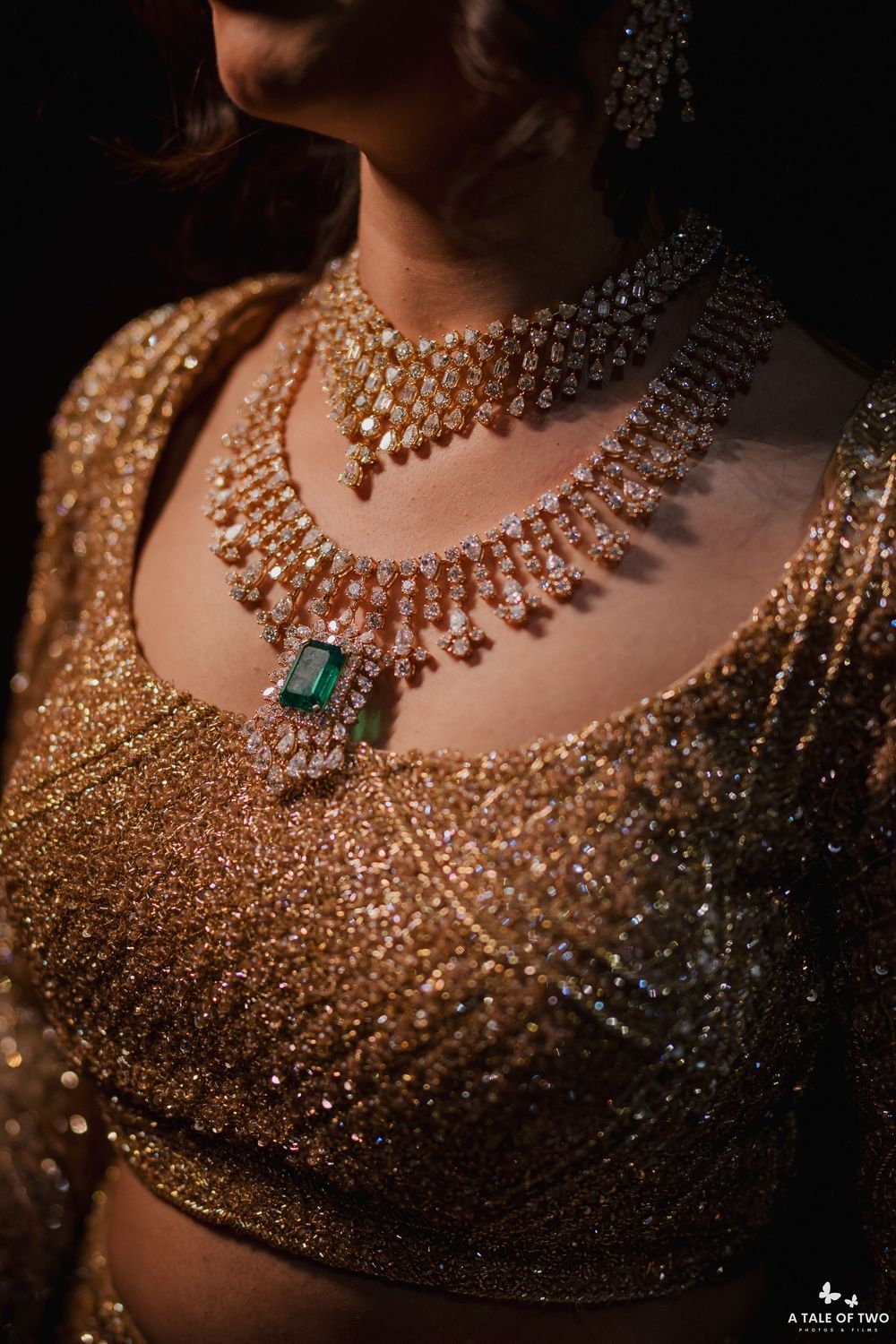 Close-up of ornate diamond and emerald bridal necklaces layered over a sparkling gold sequined blouse.