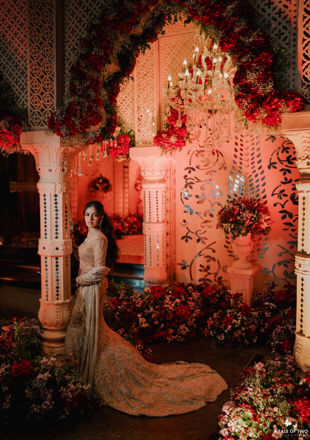 Elegant evening scene with ornate pillars, crystal chandeliers and red floral arrangements creating a romantic ambiance.