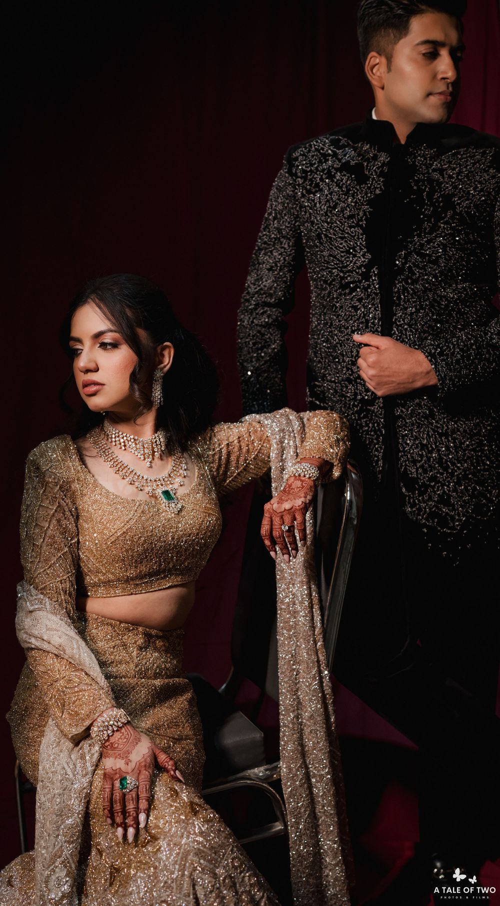 Elegant couple in glamorous gold sequined formal wear pose dramatically against dark background in artistic photoshoot.