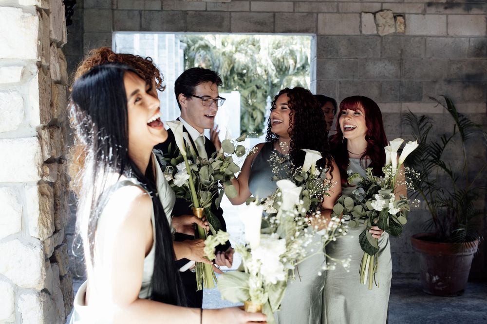 Wedding party celebrates joyfully with white floral arrangements in an elegant indoor setting.