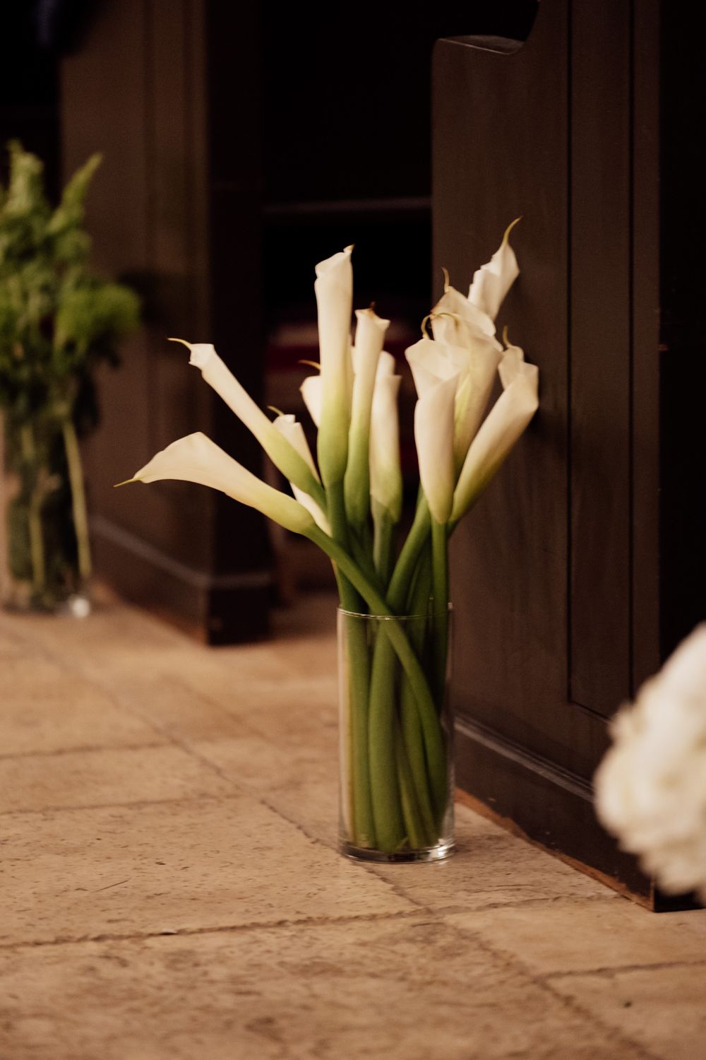 White calla lilies in glass vases arranged in a row on a wooden surface with dark background.
