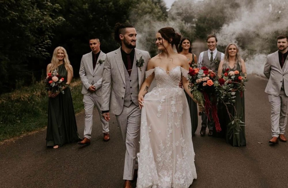 A romantic outdoor wedding celebration with guests gathered on a wooded path during golden hour.
