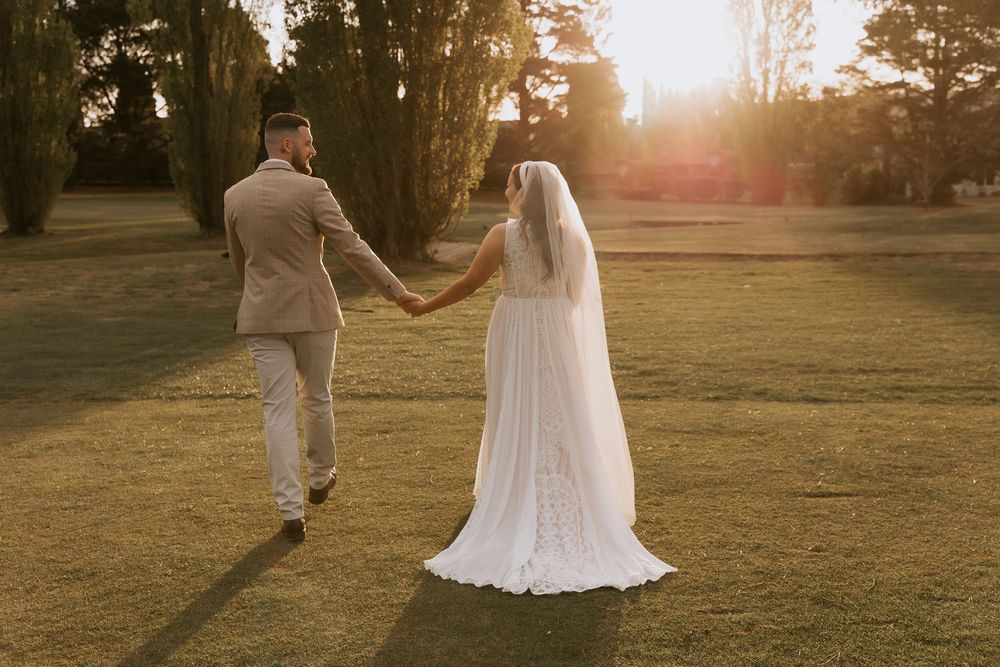 A couple in wedding attire dances together in a sunlit field during golden hour at sunset.