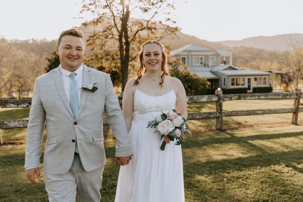A couple stands together on a sunny autumn day at their outdoor wedding ceremony with mountains in the background.
