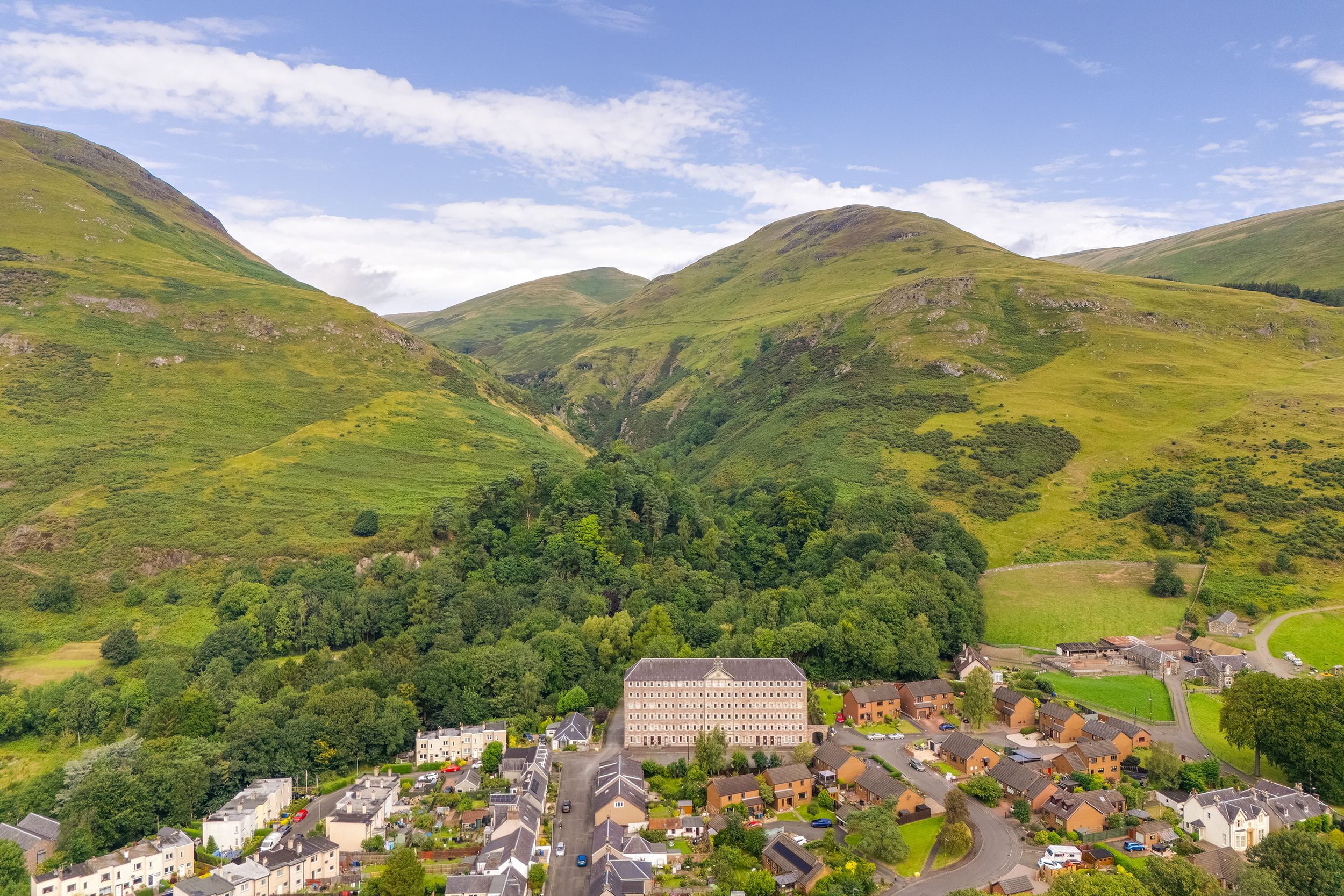 Panoramic view of a charming Scottish village nestled in the rolling green hills of clackmannanshire under blue skies.