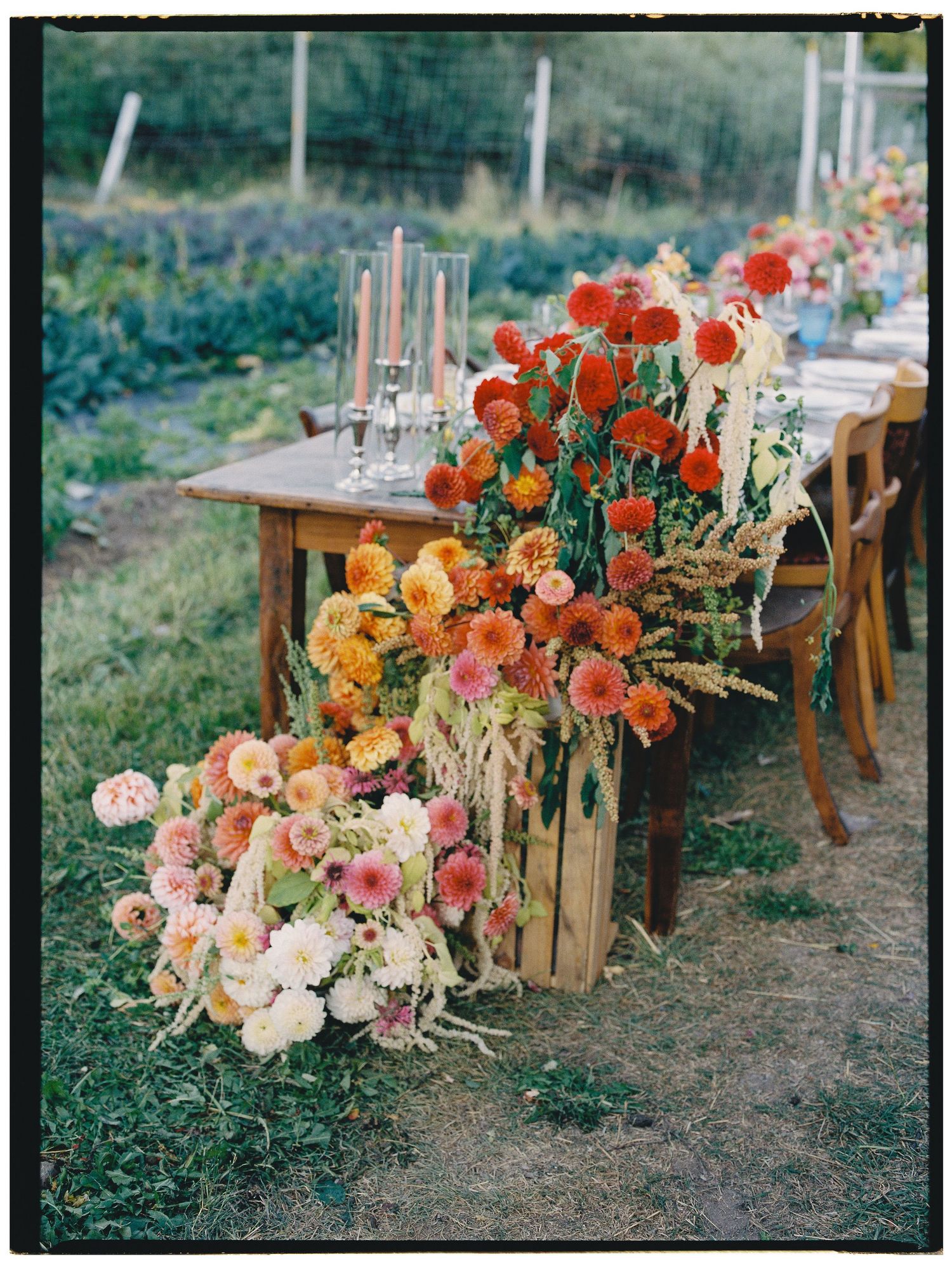 A rustic outdoor dining setup with cascading peach, coral, and orange floral arrangements adorning wooden farm tables.