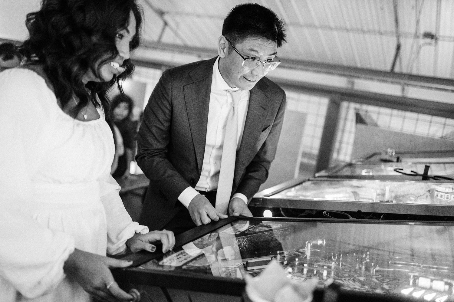 black and white photo of bride and groom playing pinball on wedding day