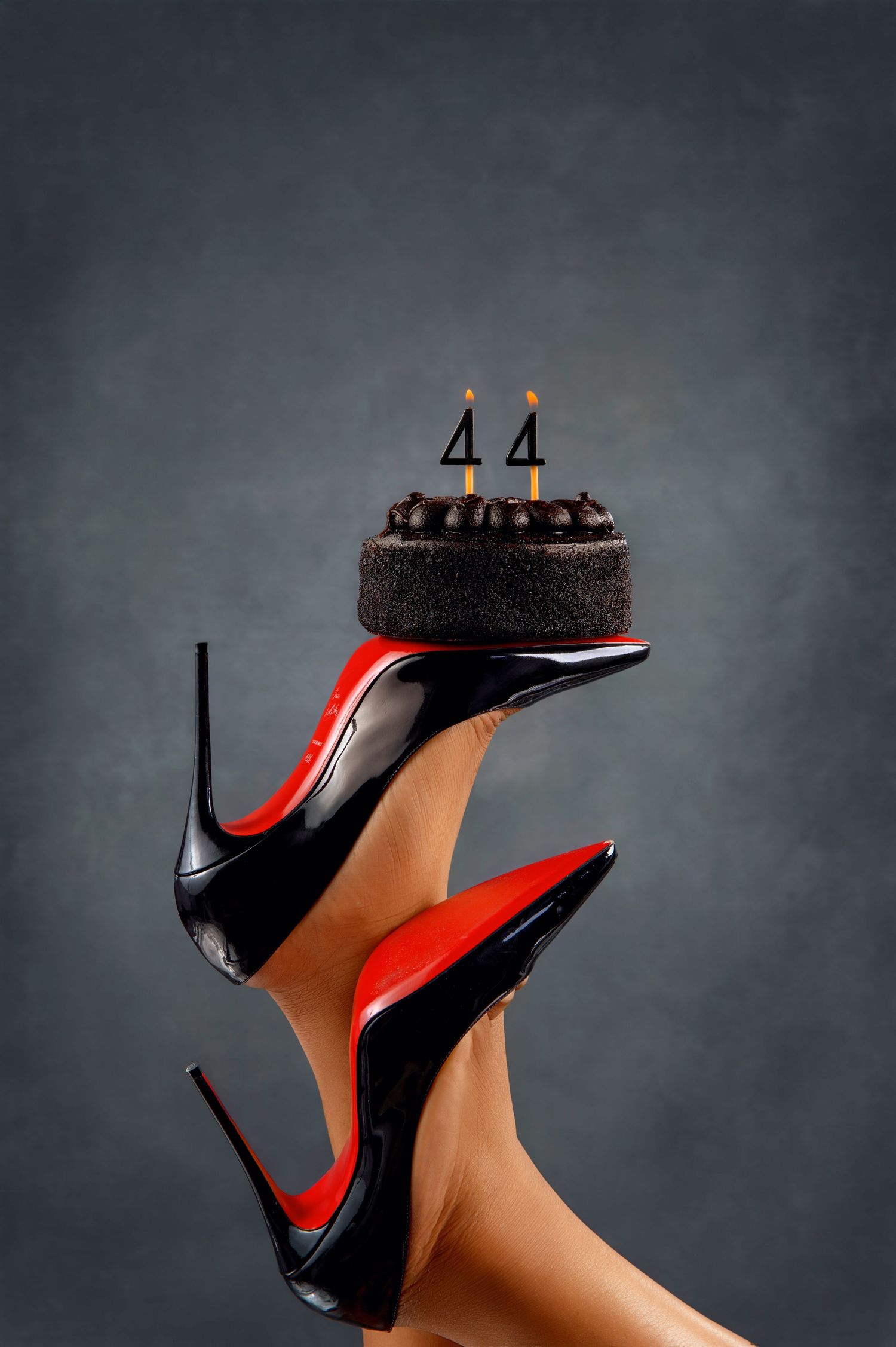 Creative still life of black high heel shoe balancing chocolate cake on grey background.