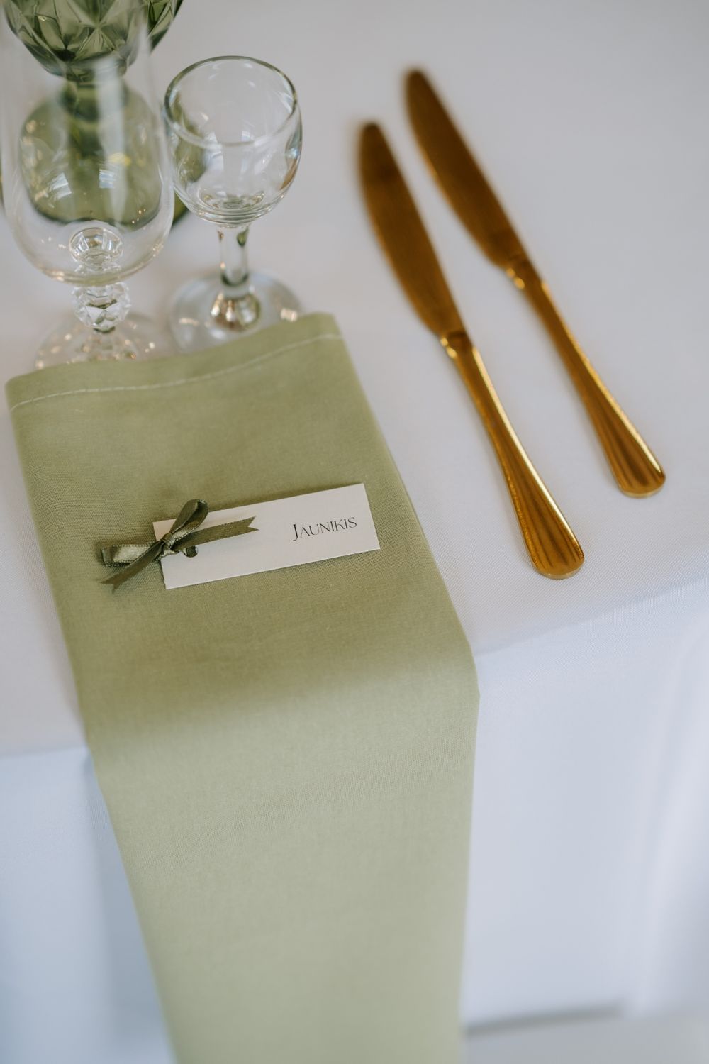 Wedding place settings with sage green napkins and gold cutlery on white tablecloths.