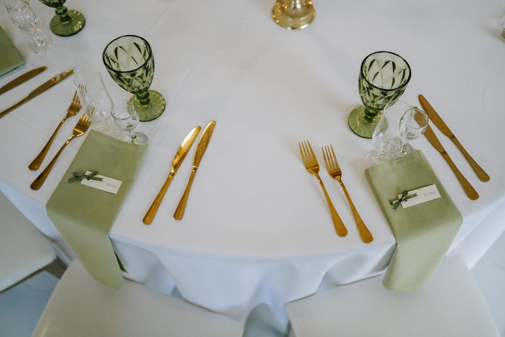 Overhead view of wedding reception table settings with green glassware and gold utensils.