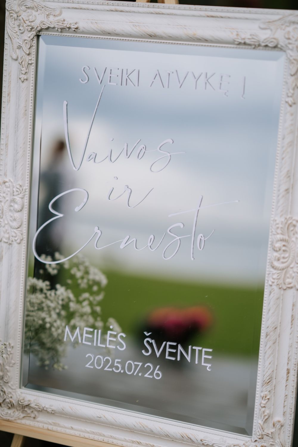 Ornate white-framed mirror with wedding details written in elegant calligraphy.