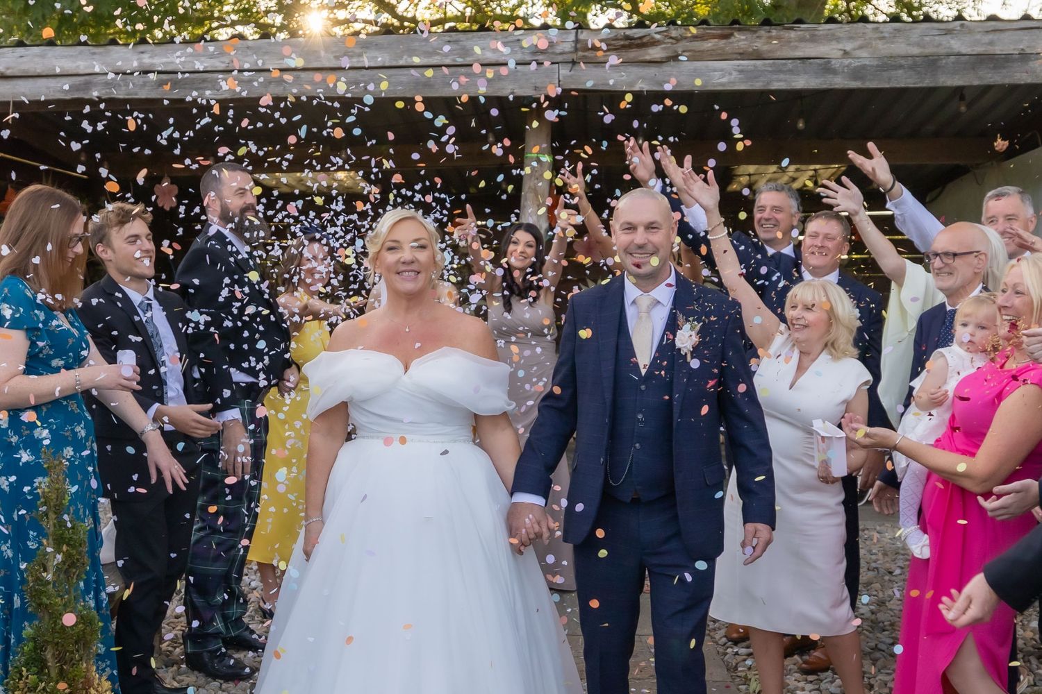 Wedding couple walking through a field while white flower petals float in the air around them on a sunny day.